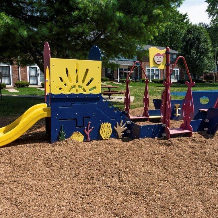 Blue, yellow, and red play gym for smaller children on light brown mulch